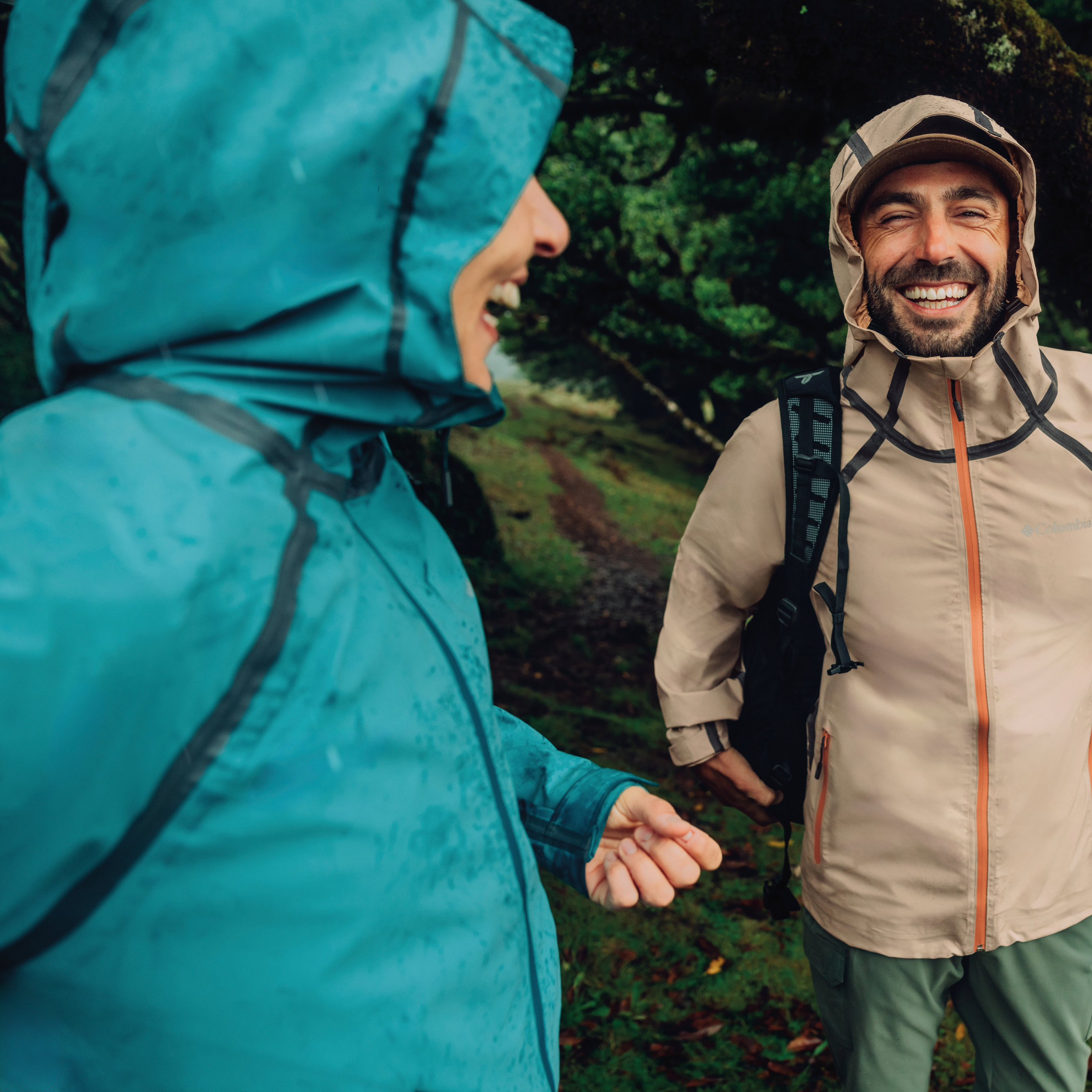 Two people in raincoats standing in a forest. Woman wearing Columbia Women's Reign No Shine Outdry Extreme Waterproof Jacket River Blue 364 2116293