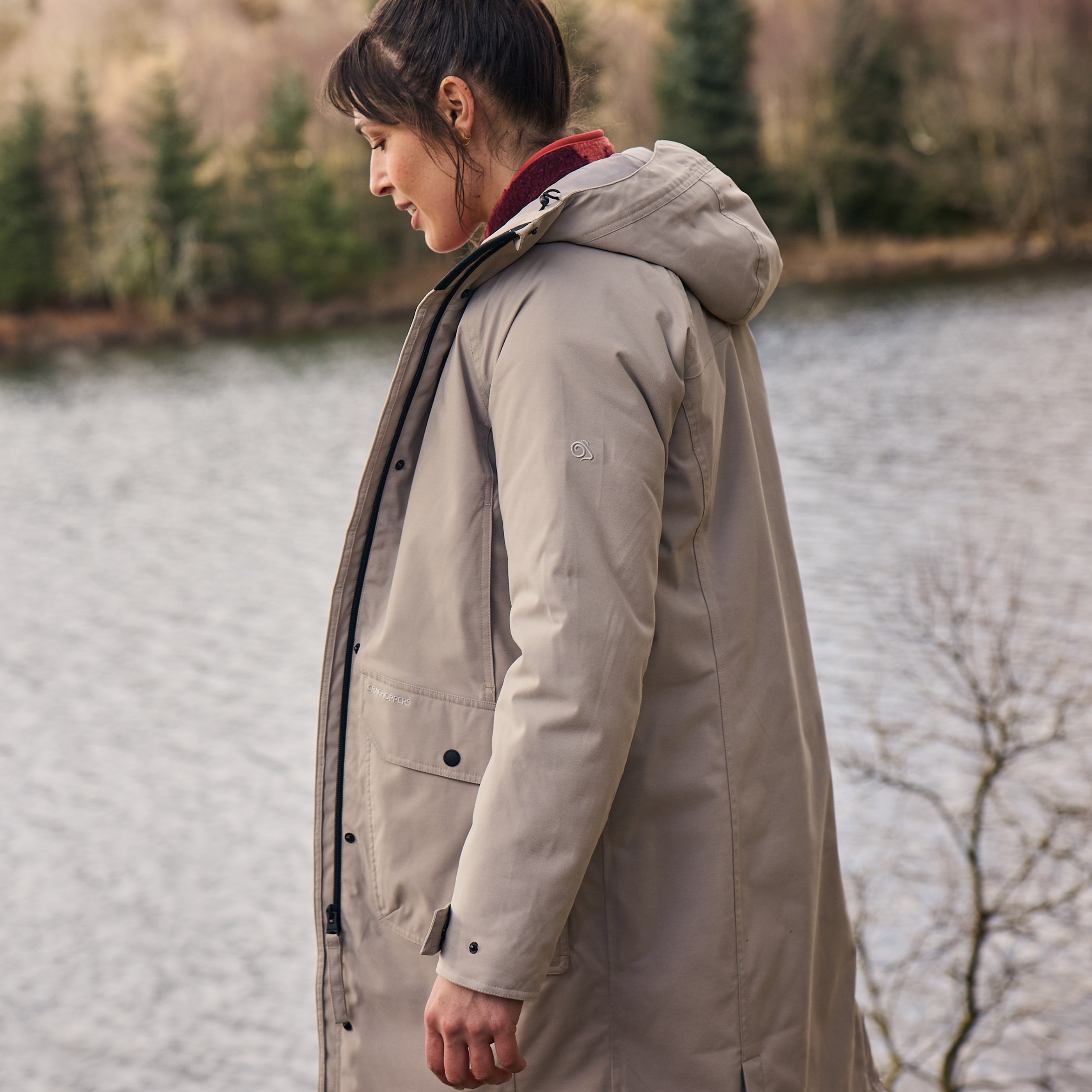 Woman wearing Craghoppers Women's Rosalind II Waterproof Insulated Parka Soft Mushroom KD7 CWP1061 with a  river in the background