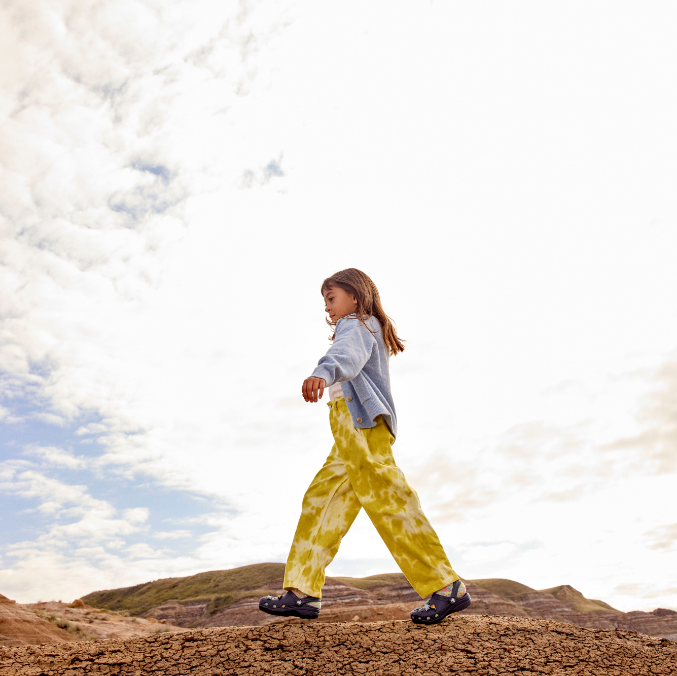 Young girl wearing Crocs Classic Clogs Junior Navy 410 206991 walking in a desert setting