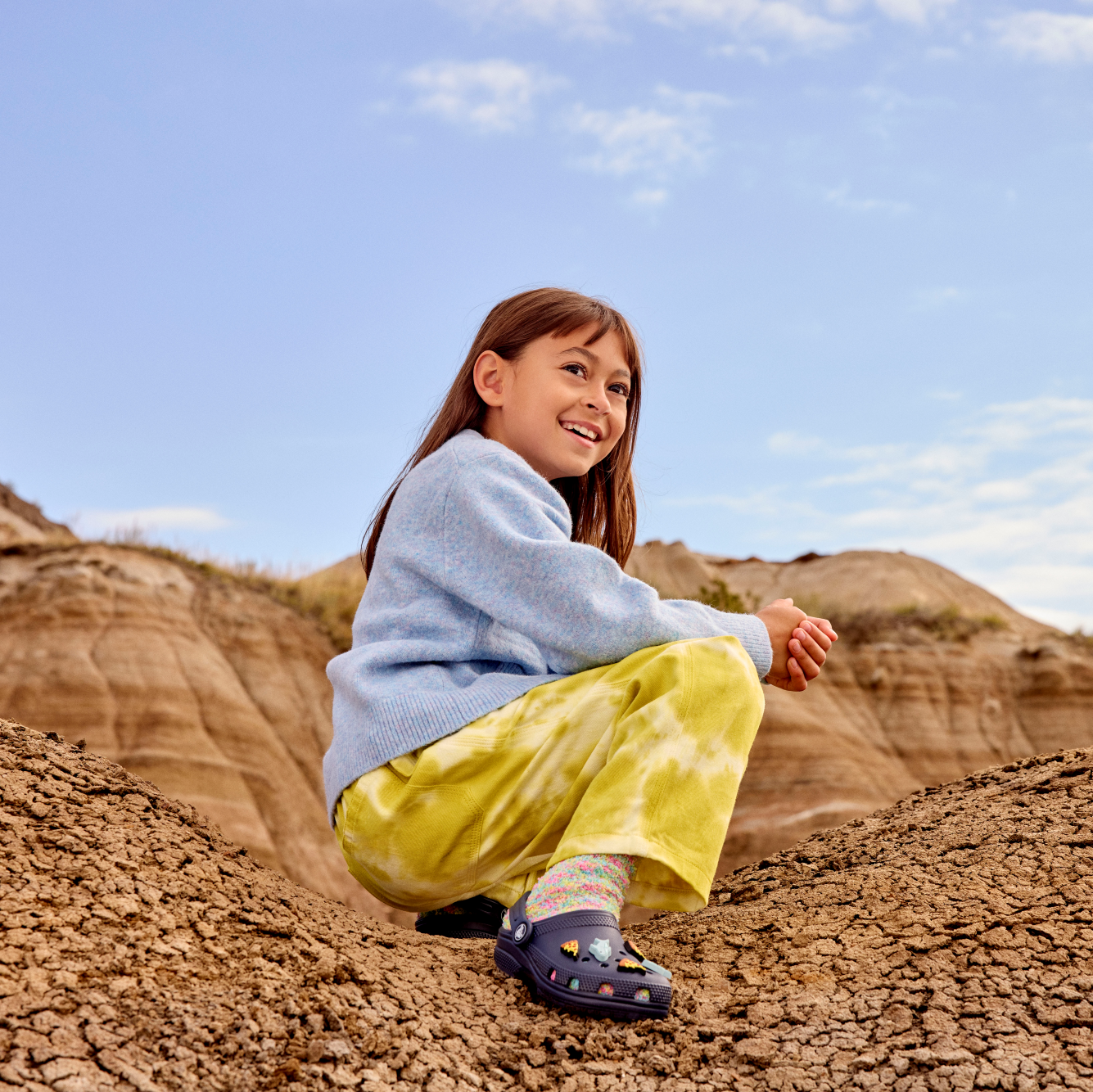 Young girl wearing Crocs Classic Clogs Junior Navy 410 206991 sitting in a desert setting