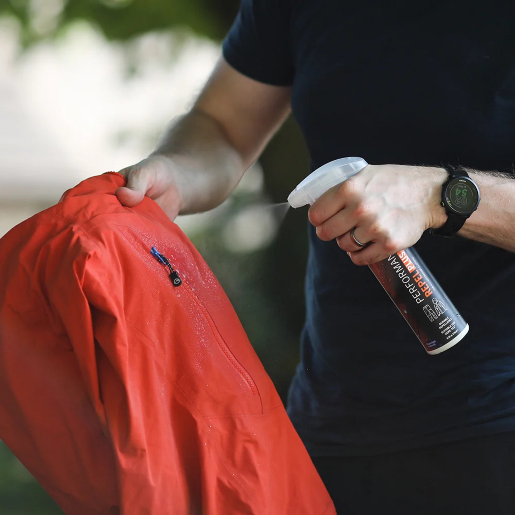 Person spraying Grangers Performance Repel Plus 275ml GRF150 on a waterproof jacket
