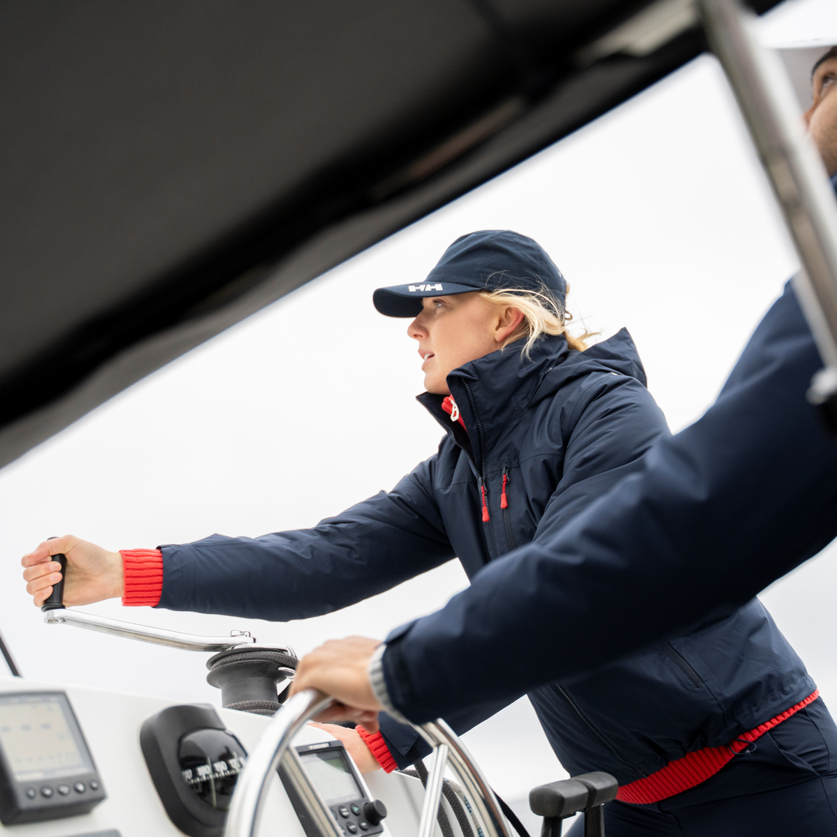 Person steering a boat wearing a Helly Hansen Women's Crew Hooded Midlayer Waterproof Insulated Jacket 2.0 Navy 597 34447