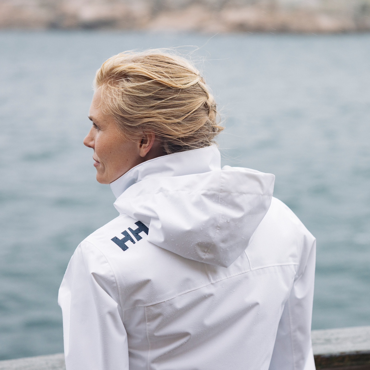 Woman looking out to sea wearing a Helly Hansen Women's Crew Hooded Midlayer Waterproof Insulated Jacket 2.0 White 001 34447