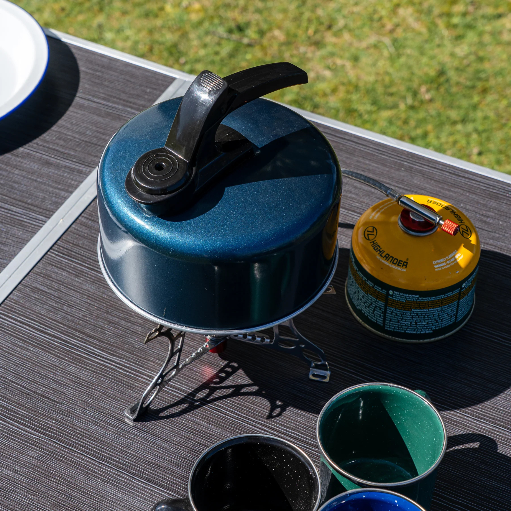 Highlander Aluminium Whistling Kettle 1L Navy CP093 Being used on a camping table on a gas stove travel stove