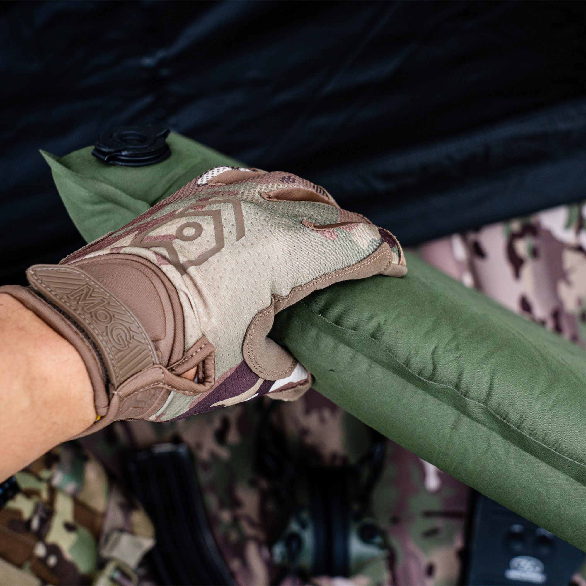 Hand wearing a tactical glove holding onto Highlander Self Inflating Kip Sleeping Mat 75mm Olive Green SM132-75