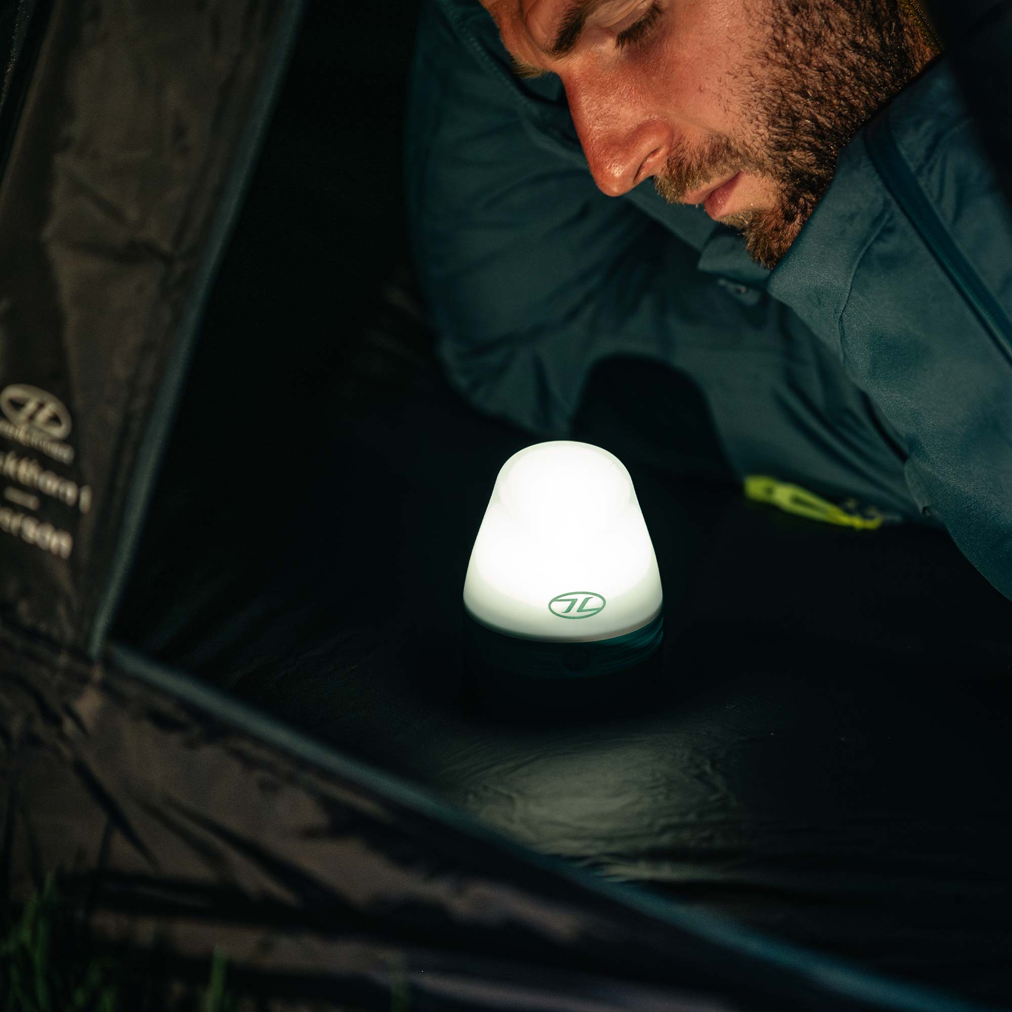Man looking at a Highlander Wee Lantern Camping Light TOR196-TL lit in a tent