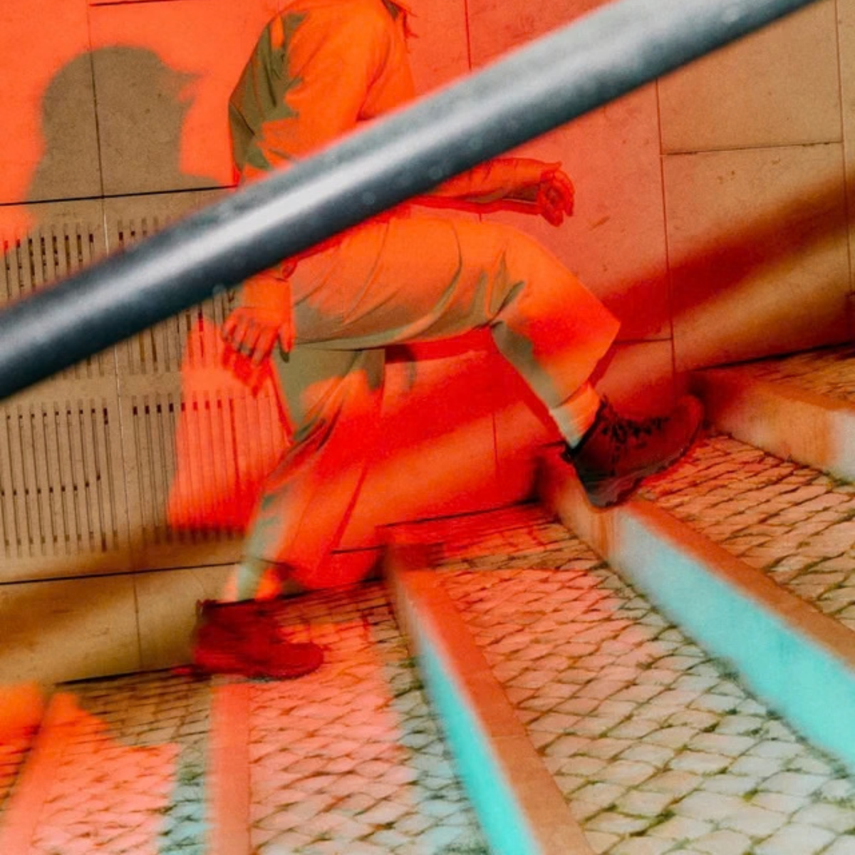 A person in light-colored clothing and Keen Men's Targhee IV Waterproof Mid Trail Boots Magnet Black 1032633 walks up stone stairs under strong red and cyan lighting, with a metal railing crossing the foreground.