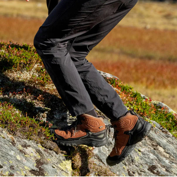 Man hiking up rocky terrain wearing Keen Men's Targhee IV Waterproof Mid Trail Boots Wide Fit Bison Black 1029002