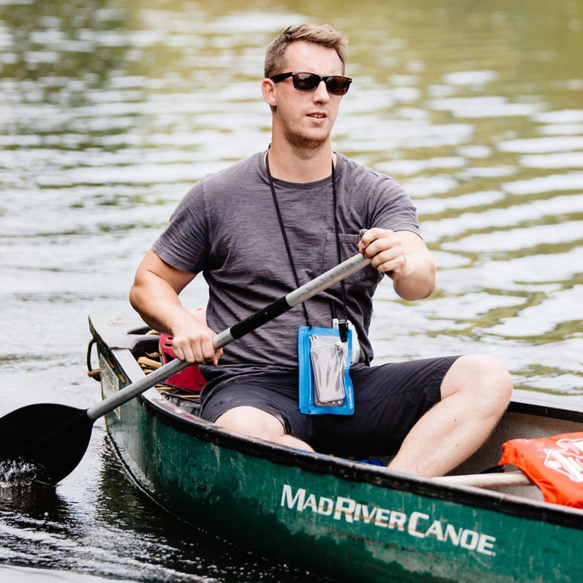 Man paddling a canoe on a body of water with a Lifeventure Hydroseal Waterproof IPX7 Phone Case Blue 59550 around his neck with a phone in it
