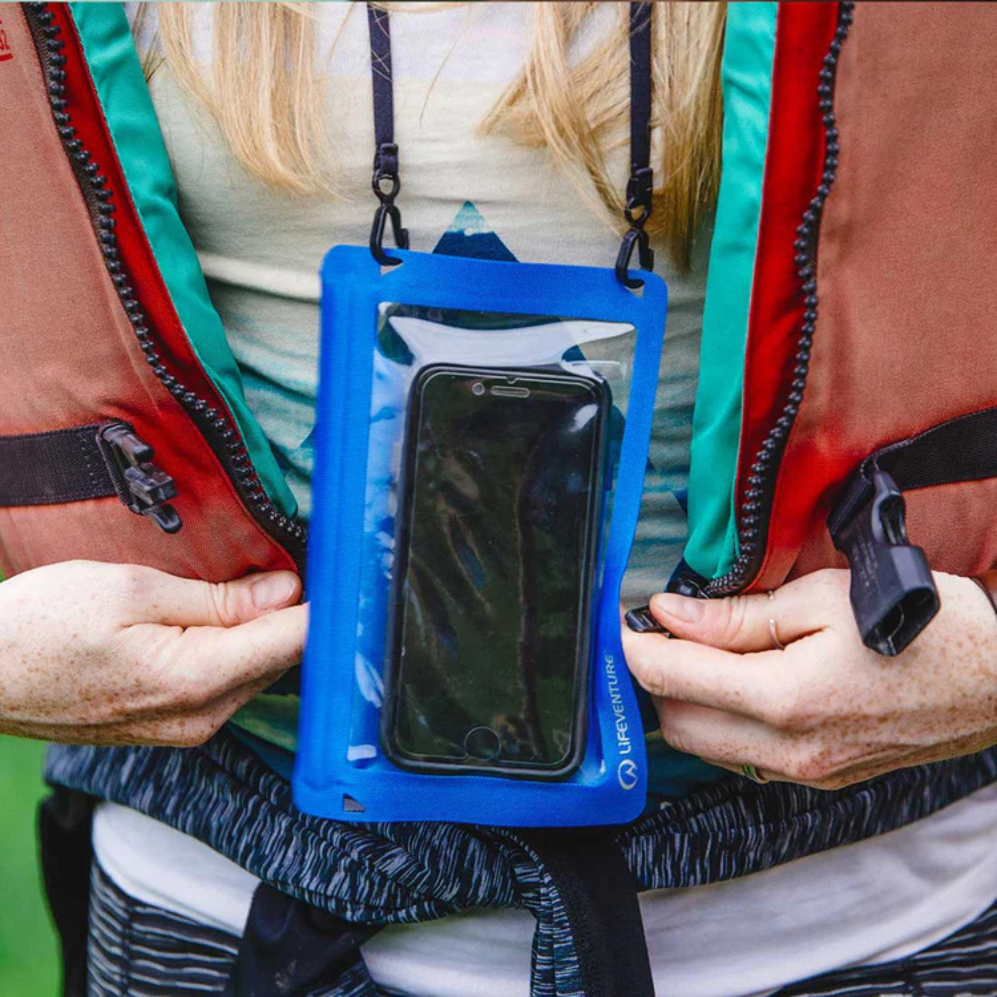 Person holding a Lifeventure Hydroseal Waterproof IPX7 Phone Case Blue 59550 with a phone inside, putting on a buoyancy aid.