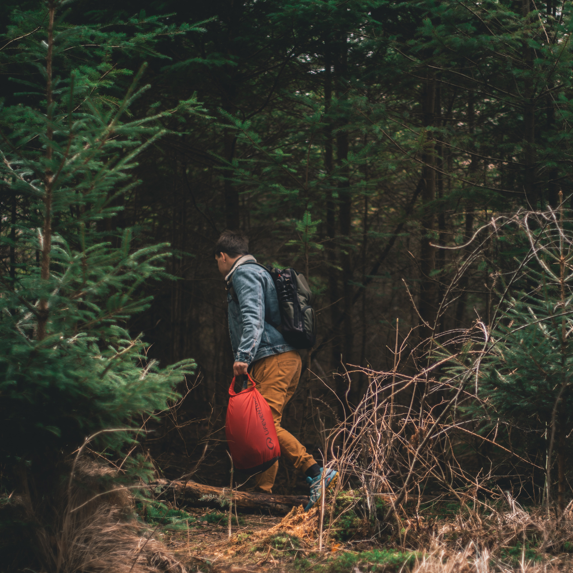 Person hiking through a forest carrying a red Lifeventure Ultralight Dry Bag 