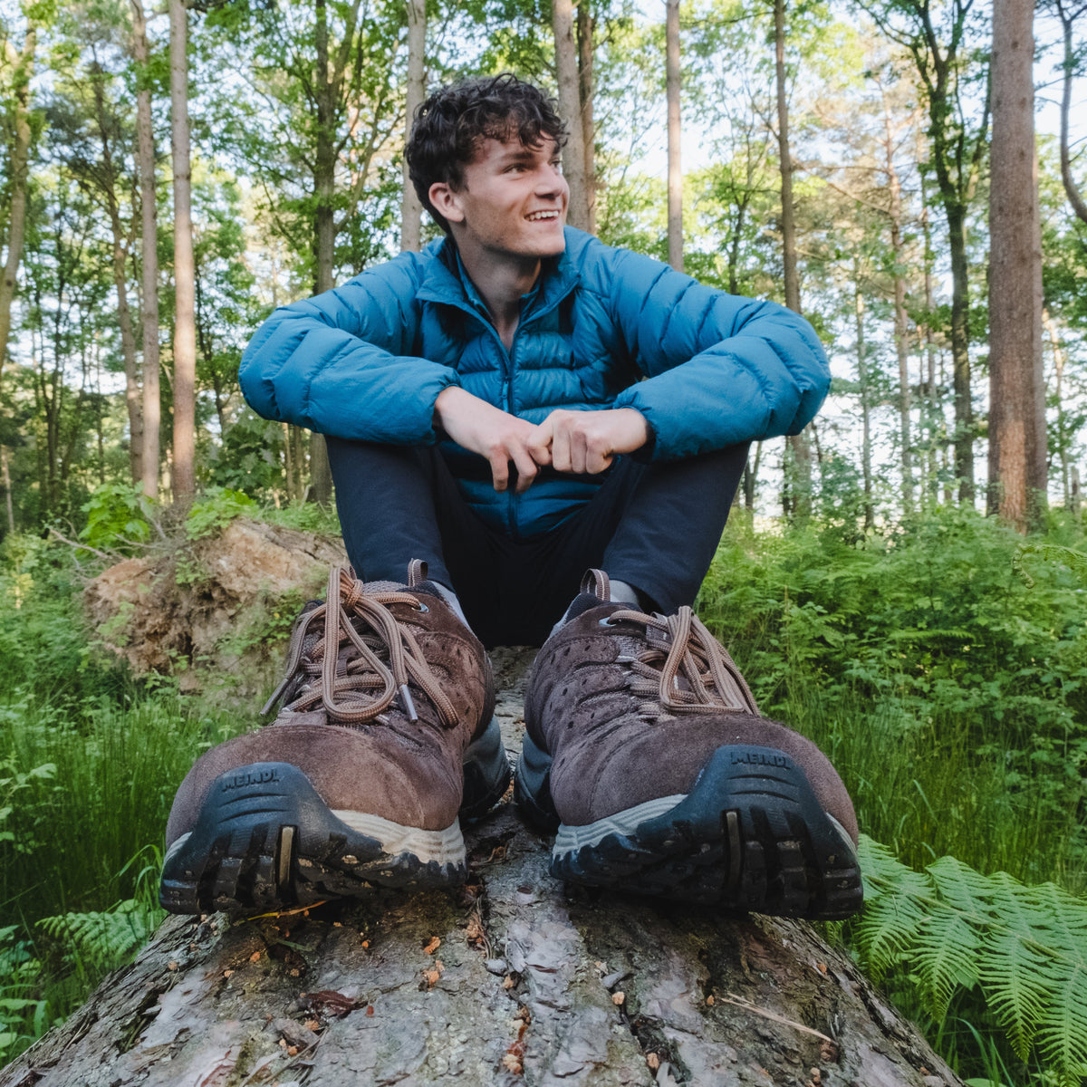 Person sitting on a log in a forest wearing Meindl Men's Rapide Gore-Tex Walking Shoes Wide Fit Dark Brown 46 MEINDL5212 and a blue jacket.