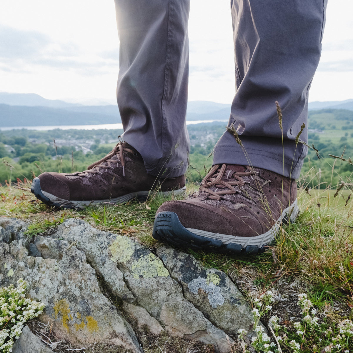 Person wearing Meindl Men's Rapide Gore-Tex Walking Shoes Wide Fit Dark Brown 46 MEINDL5212 on a rocky outcrop with a scenic view in the background