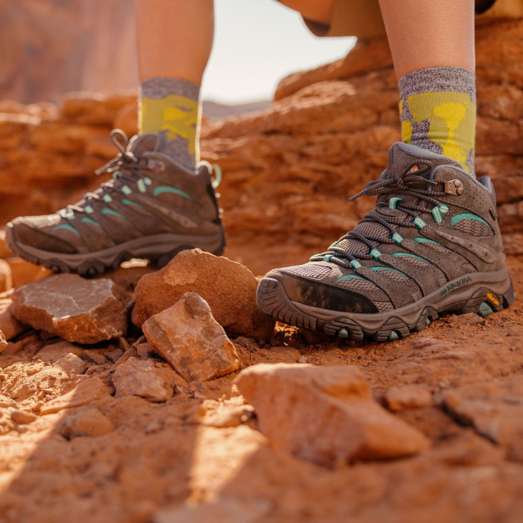 Woman sitting on a rock in a rocky desert setting wearing yellow hiking socks and Merrell Women’s Moab 3 Mid Gore-Tex Hiking Boots Sedona Sage J036306