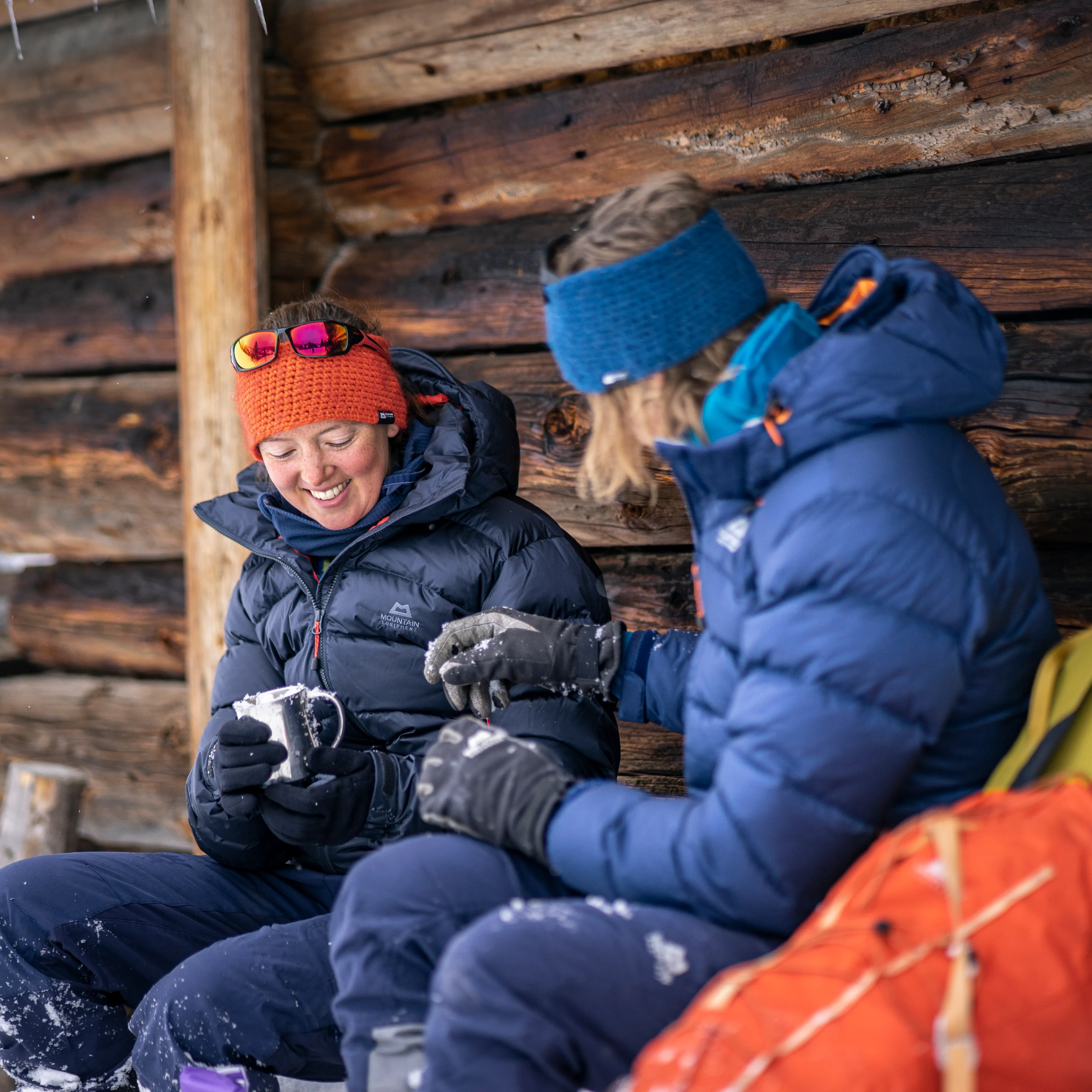 Woman wearing a Mountain Equipment Women's Lightline Down Insulated Jacket ME-01286 Cosmos ME-008590, sitting in front of a cabin in the snow
