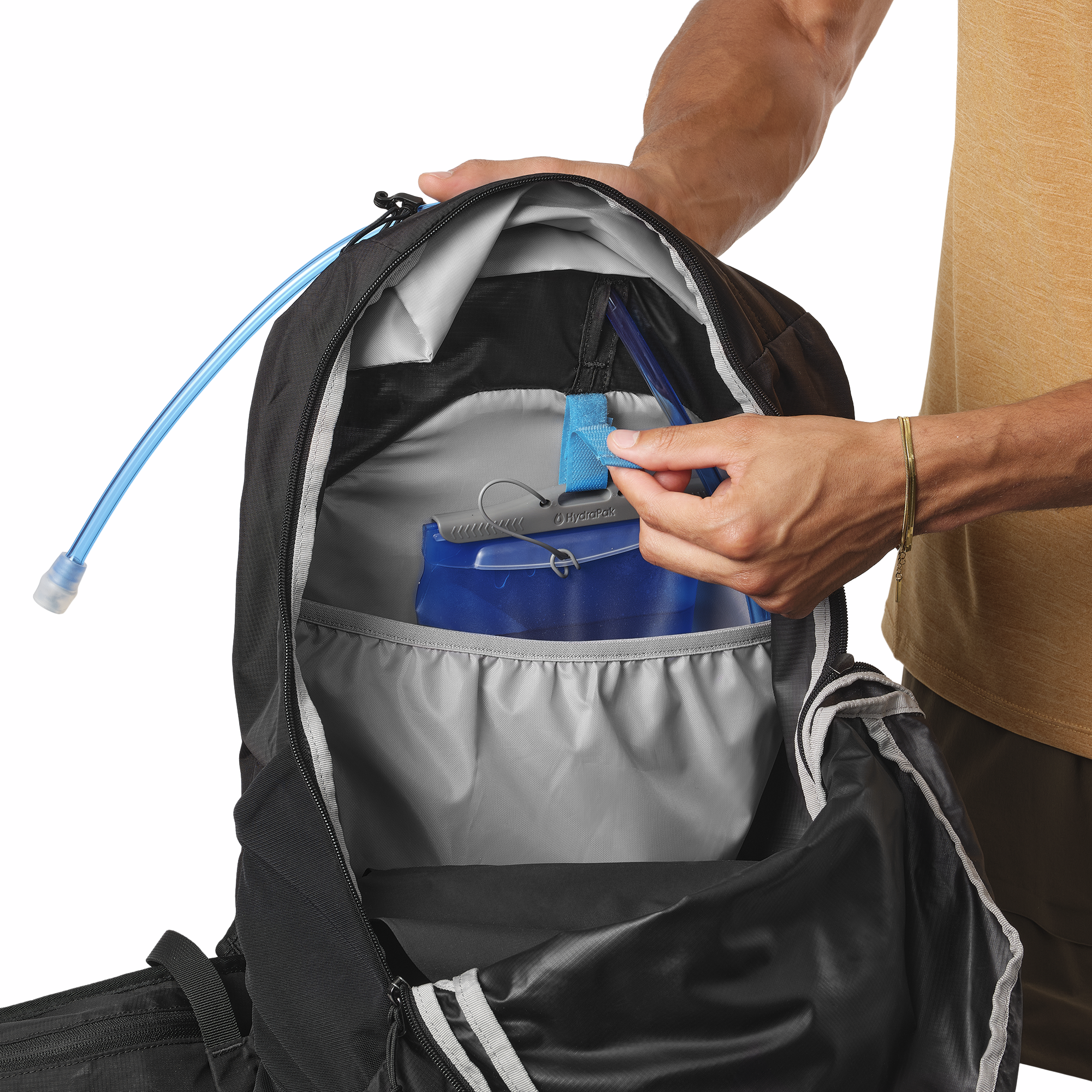 A close-up of a Salomon Trailblazer 10L Daysack Black Alloy LC2182900 being opened, with a person's hands demonstrating the use of a blue hydration reservoir inside the pack. The person's arm and torso are visible on the right side of the frame against a clean white background.
