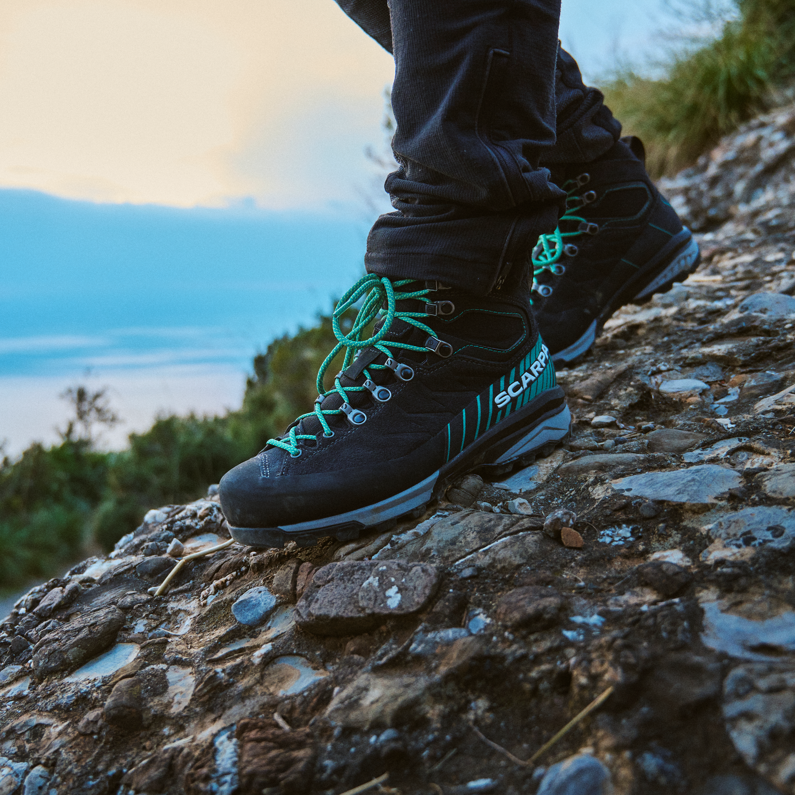Woman wearing Scarpa Women's Mescalito Trek Gore-Tex Mountaineering Boots Dark Anthracite Tropical Green 61053-202 on a rocky slope