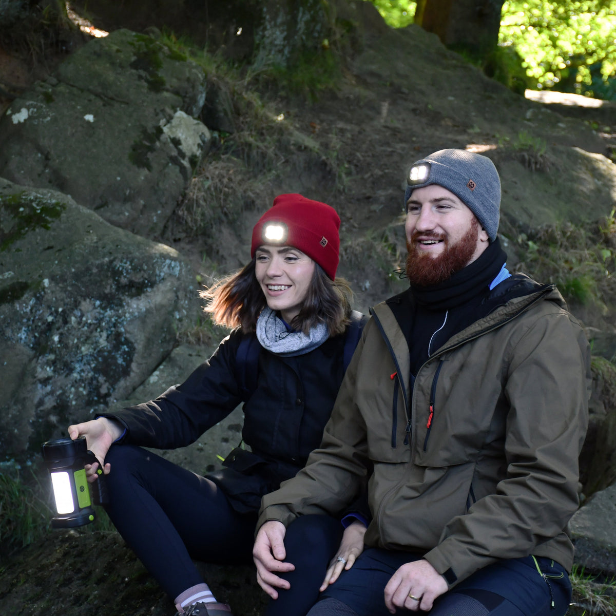 Two people sitting on rocks outdoors surrounded by nature. Man wearing Six Peaks Unisex LED Lighted Beanie Hat Grey SIH0004