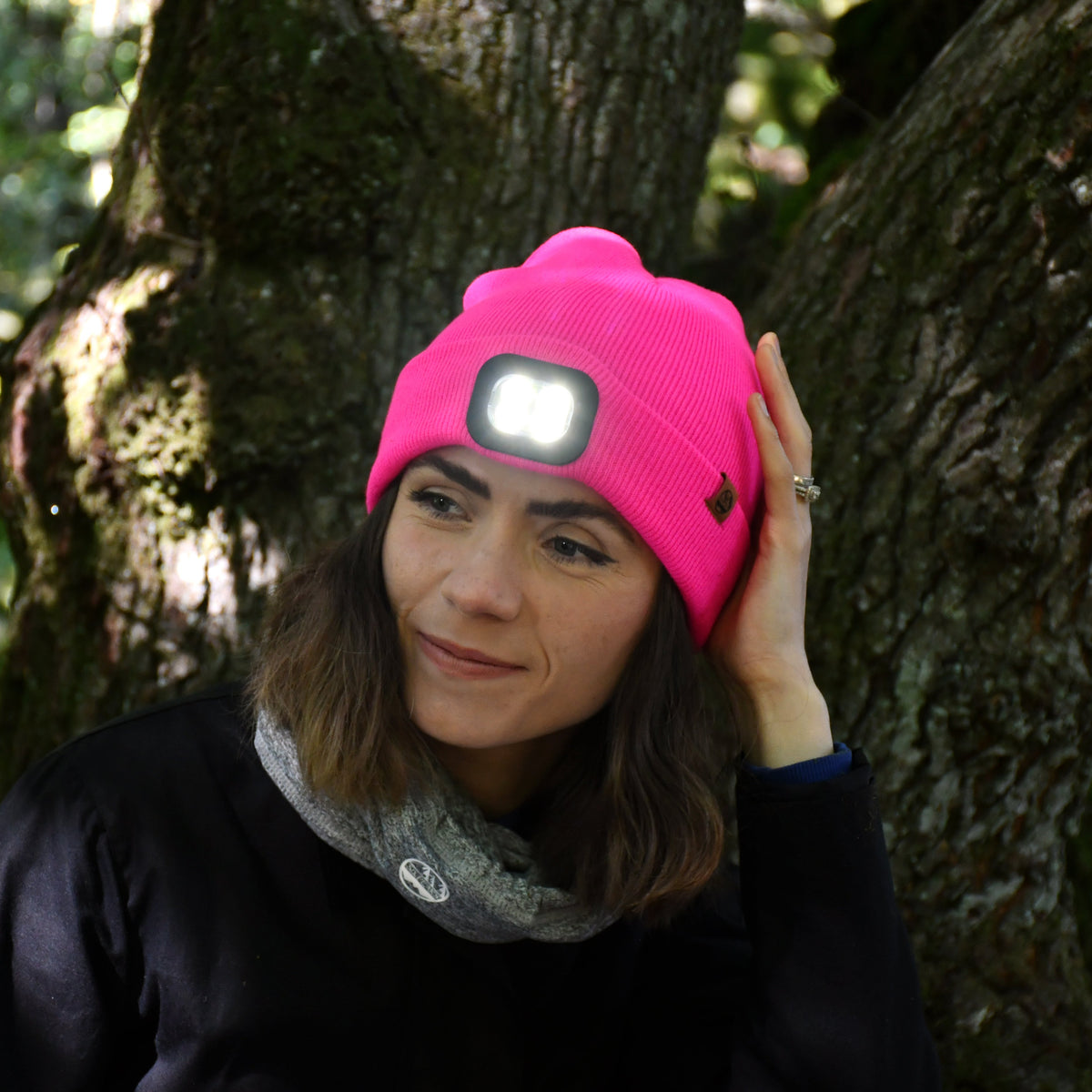 Woman Six Peaks Unisex LED Lighted Beanie Hat Pink SIH0004 leaning against a tree