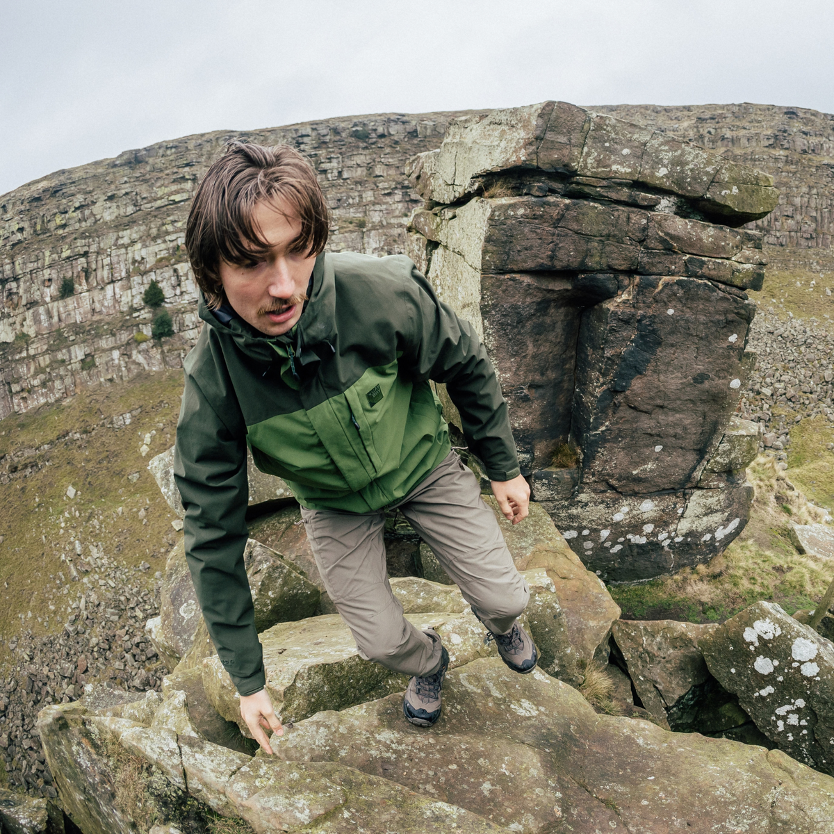 Man wearing a Sprayway Men's Santiago InterActive Waterproof Jacket SP-01753 Cypress Forest SP-008867 hiking across boulders