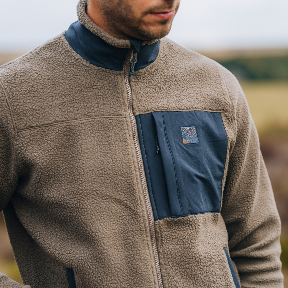 A close-up of a man wearing a Sprayway Men's Whitle Full Zip Fleece Jacket  SP-01737 Brownstone DkGraphite SP-007561 outdoors.
