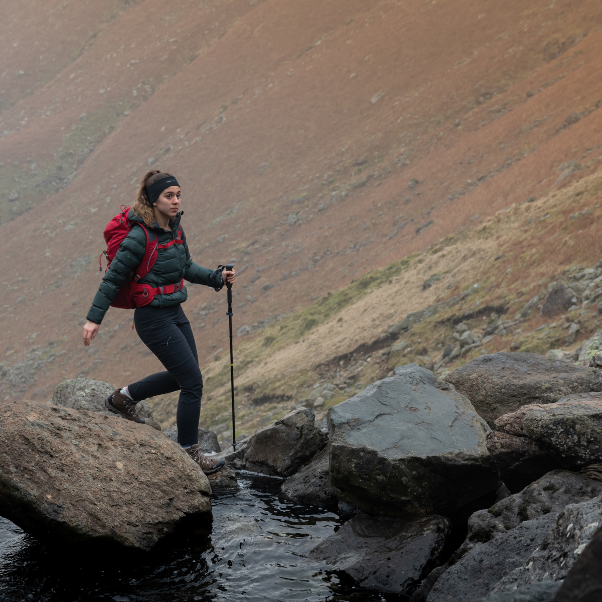 Person hiking on rocky terrain with a backpack and Trekmates Fold Lock Hiking Pole Black TM-008701
