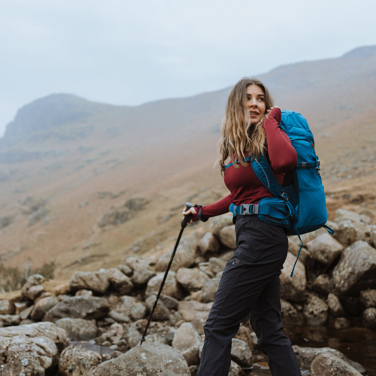 Woman hiking on a rocky path with mountains in the background using a Trekmates Hiker Shock Single Pole Black TM-008705