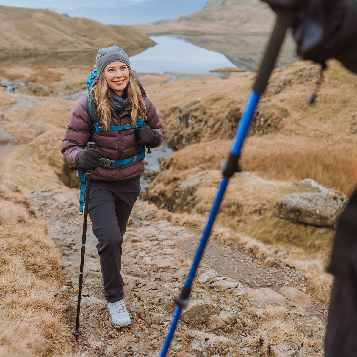 Woman hiking in a mountainous landscape with a lake in the background using a Trekmates Hiker Shock Single Pole Black TM-008705