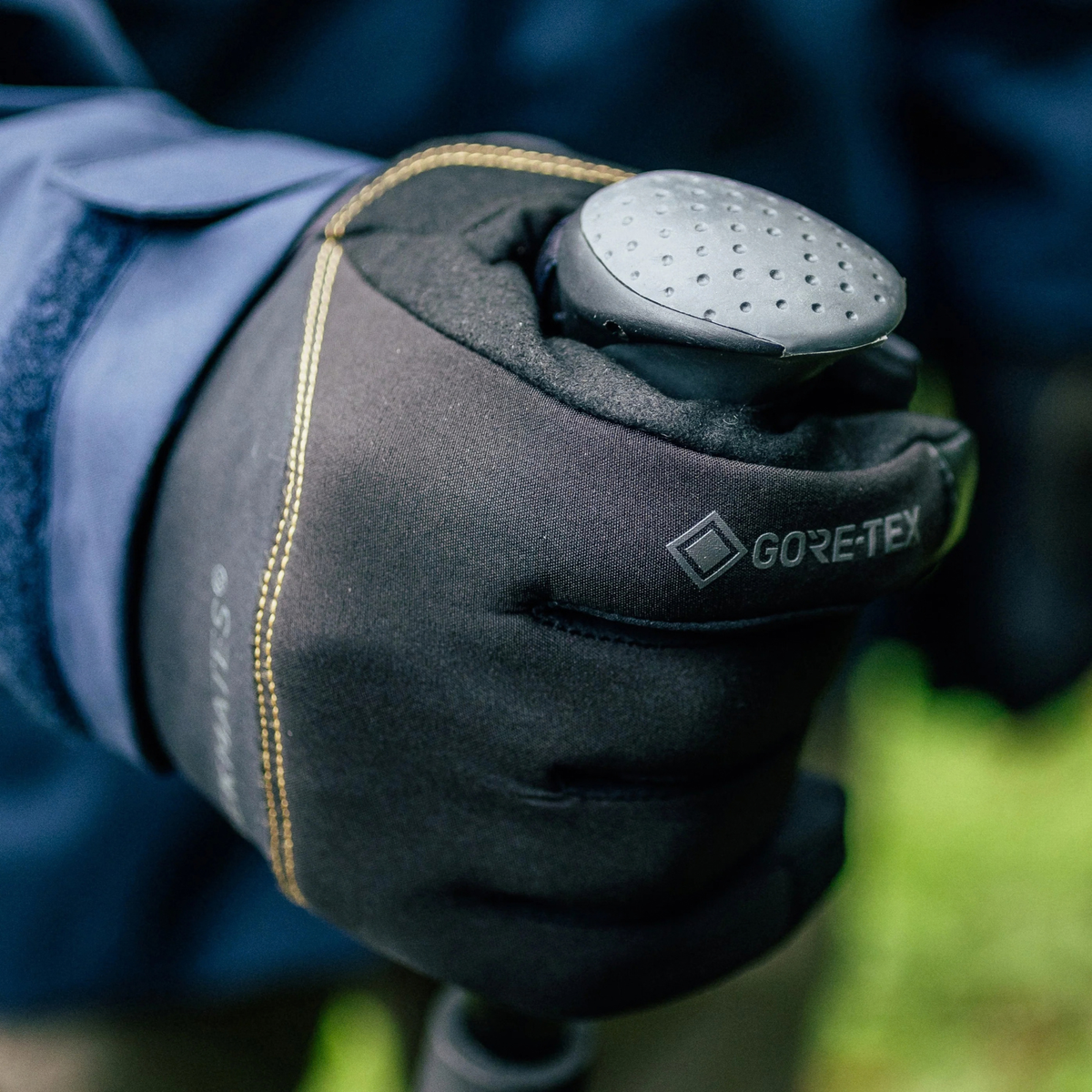 A close-up of a Trekmates Unisex Friktion Gore-Tex Waterproof Gloves Black TM-008647 worn on a hand, holding a dark grey walking pole handle.