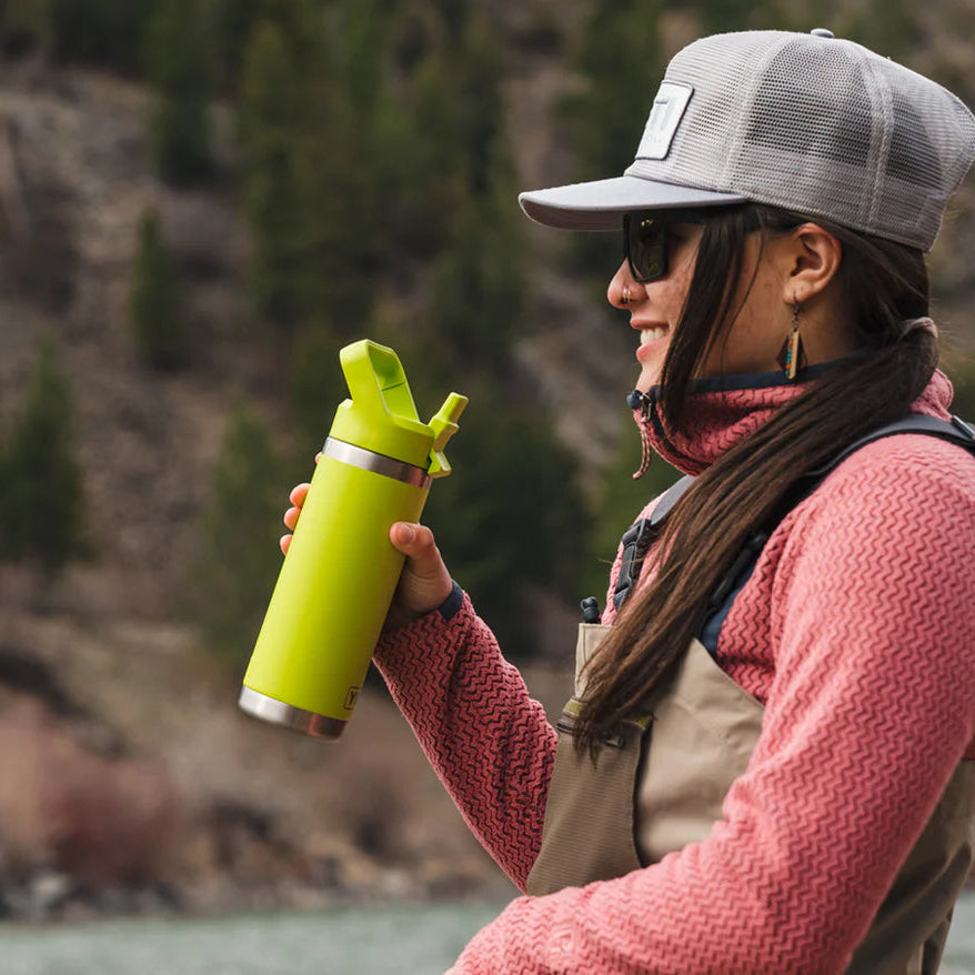 Person holding a green Yeti water bottle outdoors with a natural background