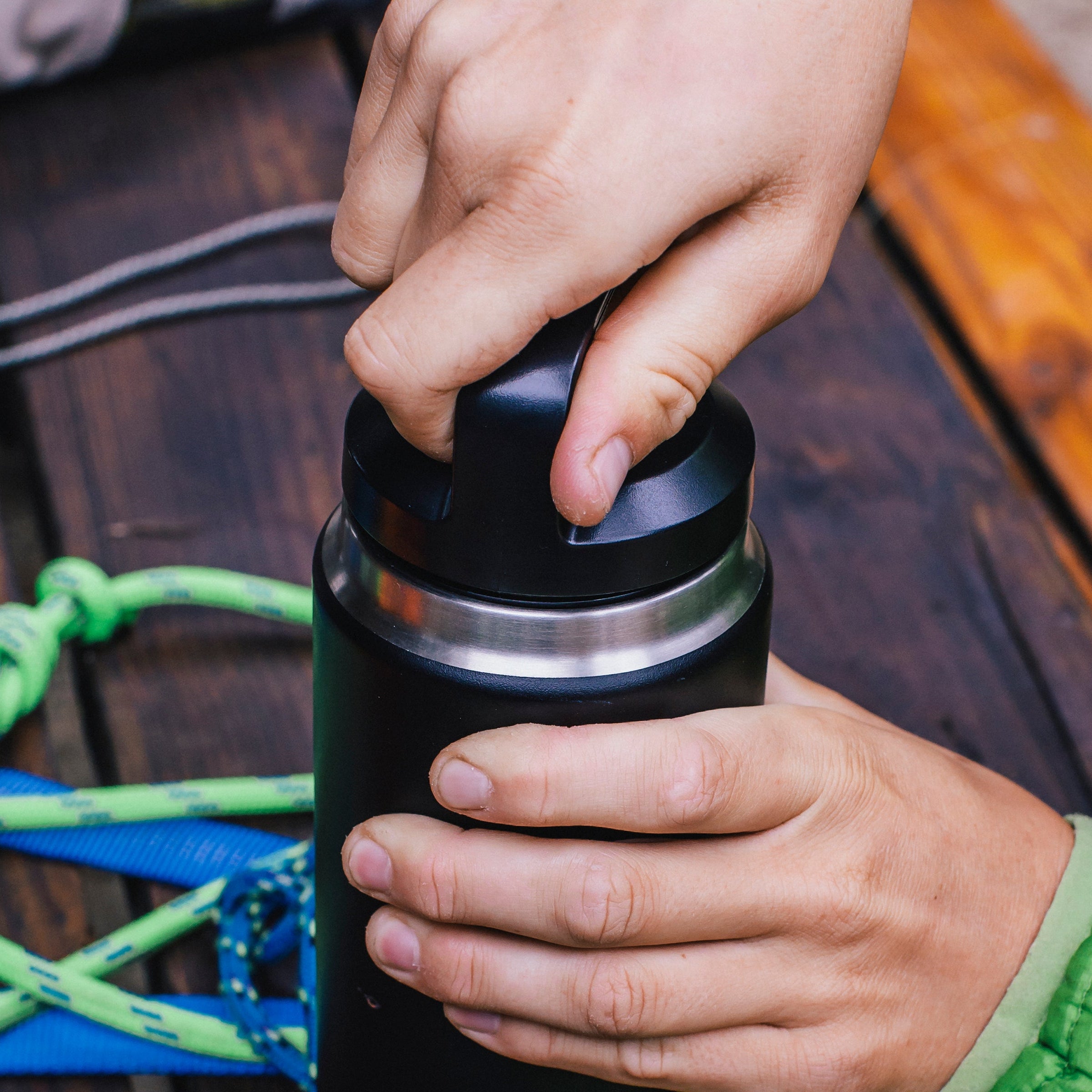 Person unscrewing the lid of a Yeti Rambler 26oz Chug Cap Bottle Yeti-Chug-26oz on a  wooden table