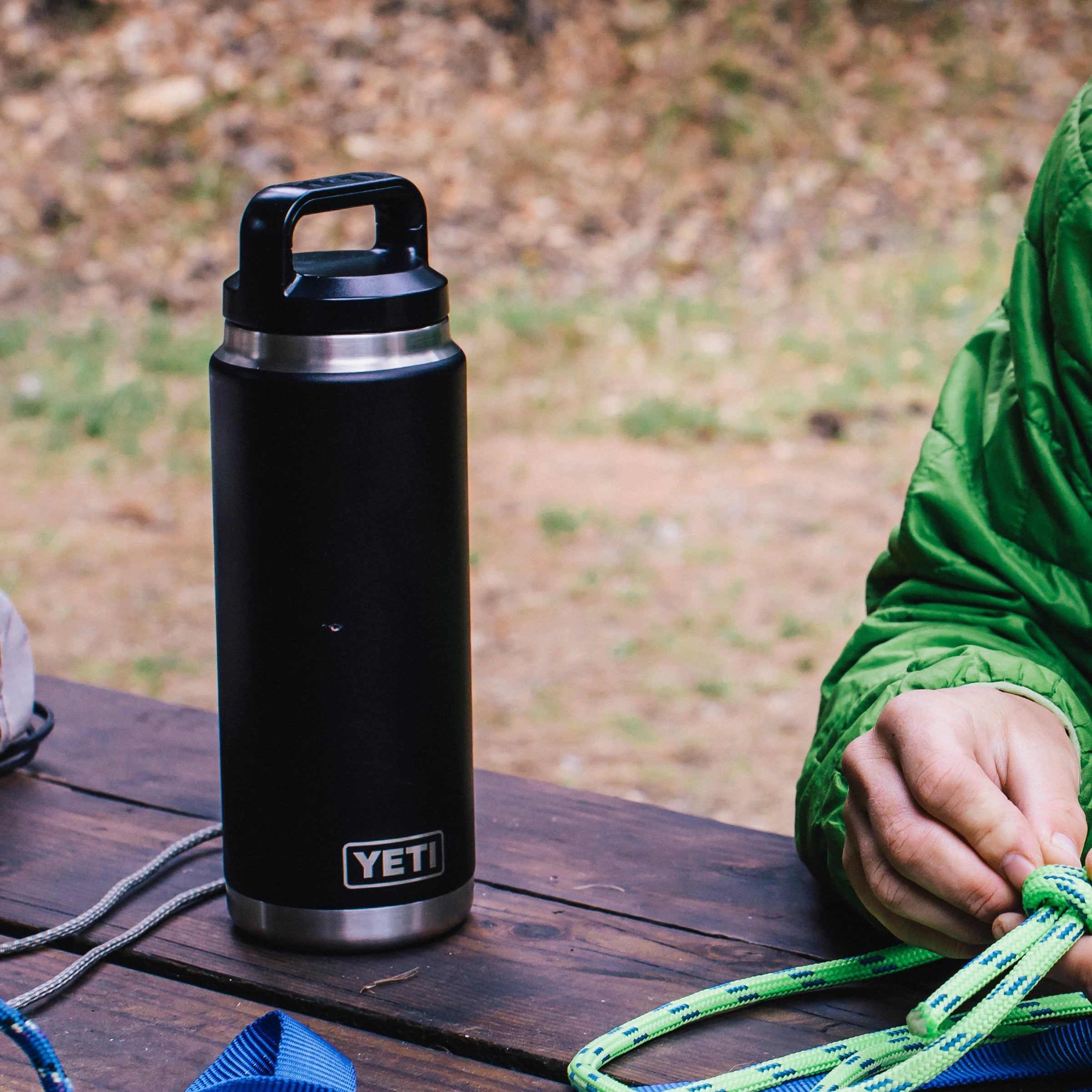 Yeti Rambler 26oz Chug Cap Bottle  Yeti-Chug-26oz on a wooden table with a person in a green jacket in the background.